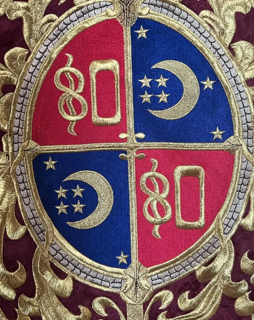 Escudo bordado en oro sobre raso rojo y azul