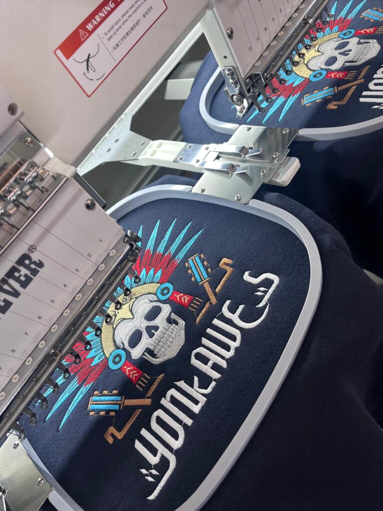Máquina de bordar de dos cabezales trabajando sobre sudaderas azul marino en el taller