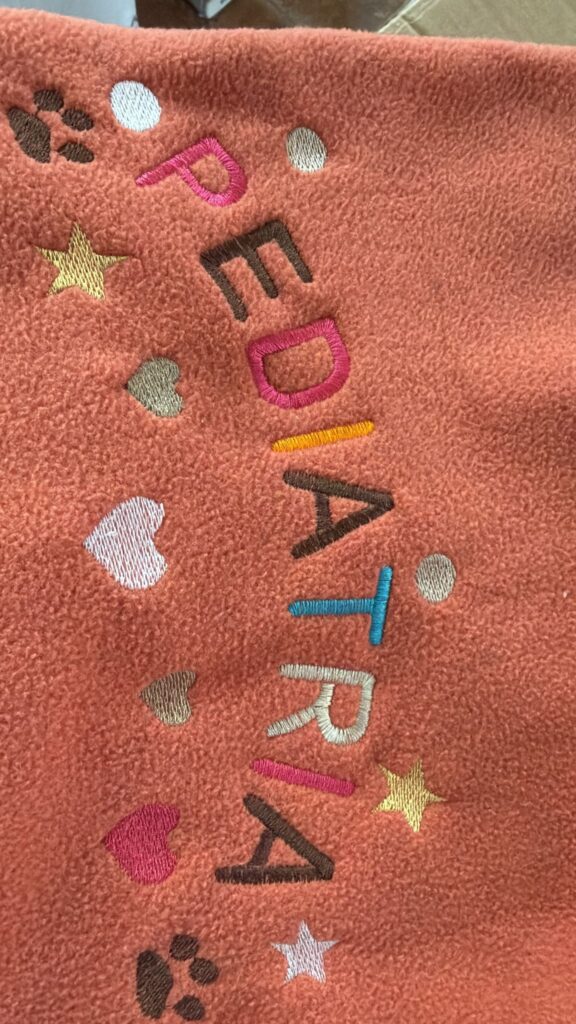 Palabra Pediatría bordada en letras de colores sobre forro polar coral