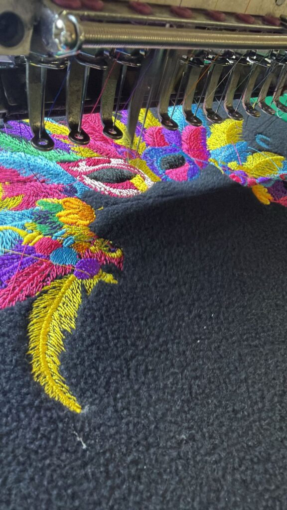 Plumas y antifaz multicolor bordándose sobre forro polar oscuro